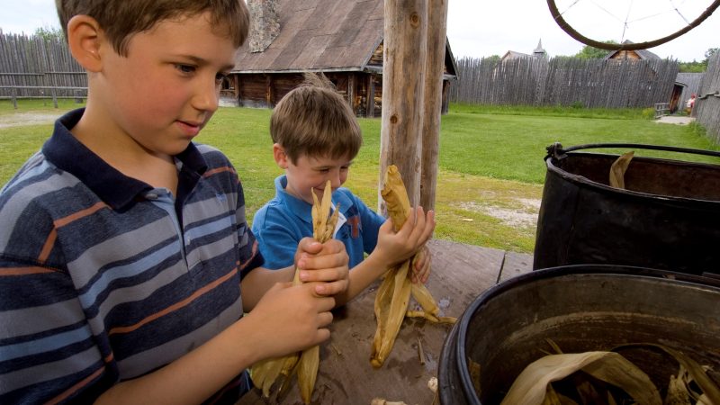 Two young visitors making corn husk dolls at Sainte-marie among the Hurons