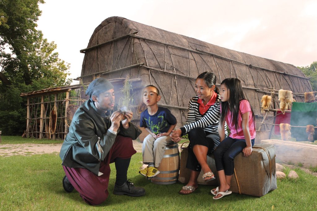 Un interprète historique costumé démontre une ancienne technique de commencer un feu, pour une famille de touristes