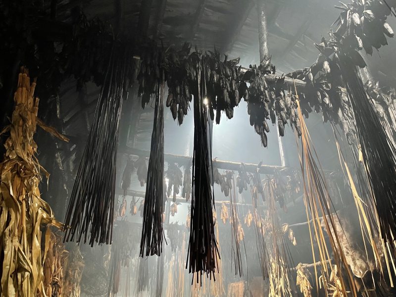 An interior shot of a longhouse at Sainte-Marie among the Hurons. The ceilings are hanging with corn, some of it blackened by smoke.