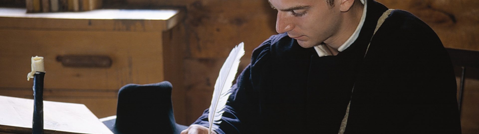 Un interprète historique, habillé en costume de jésuite, à écrire avec une plume et de l'encre.