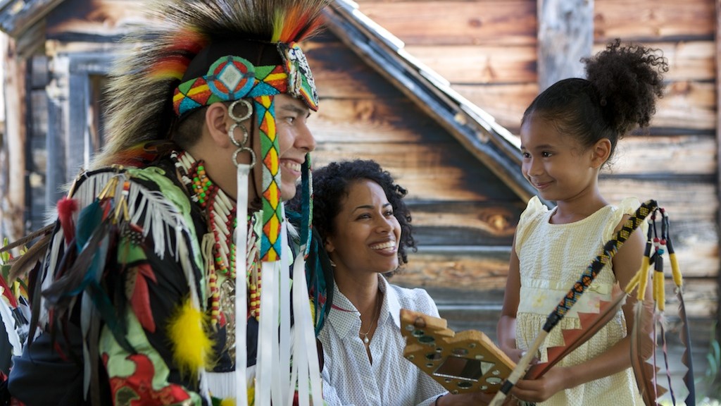 Un homme autochtone en habit cérémonial sourit à deux visiteurs