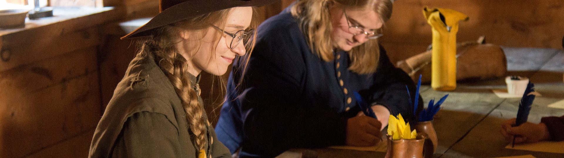 Two costumed historical interpreters practise quill pen writing at Sainte-Marie among the Hurons