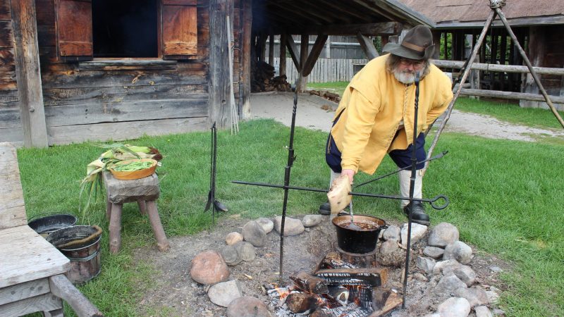Michel, un interprète historique costumé, cuisine par la chaleur d'un feu dans la cour nord de Sainte-Marie
