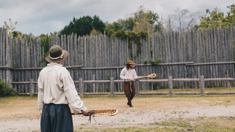 Two costumed historical interpreters playing lacrosse
