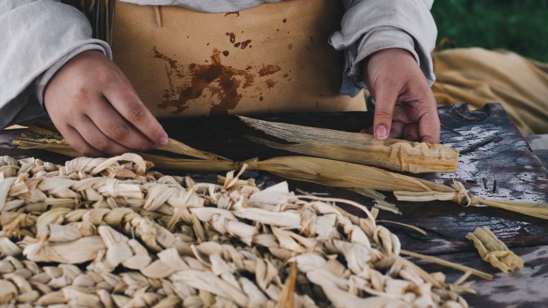 Un interprète historique tresse des épluches de maïs pour faire un tapis