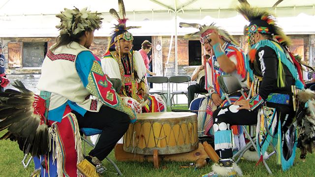 Quatres hommes autochtones en habits cérémoniaux, à jouer un gros tambour en chantant
