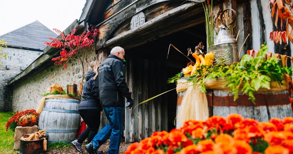 Two guests in fall coats walking through the main entrance of Sainte-Marie, which is decorated for fall with mums, sumac and gourds