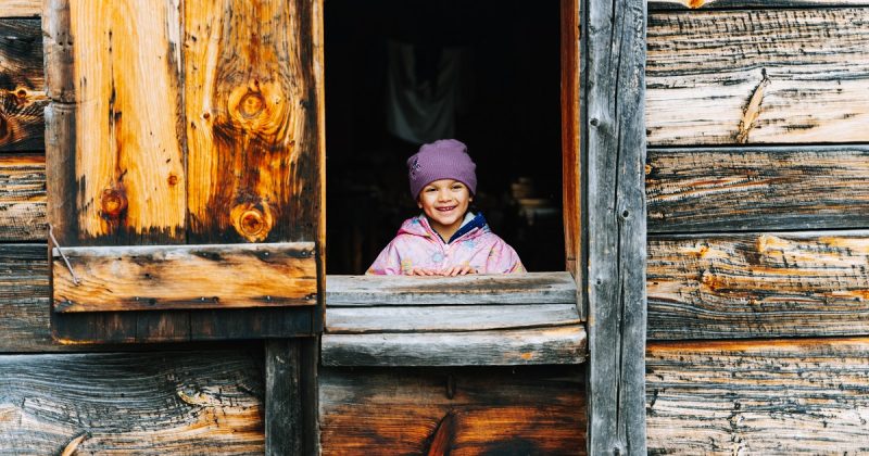 A smiling little girl looking out from inside a building at Sainte-Marie - the shutters are wide open