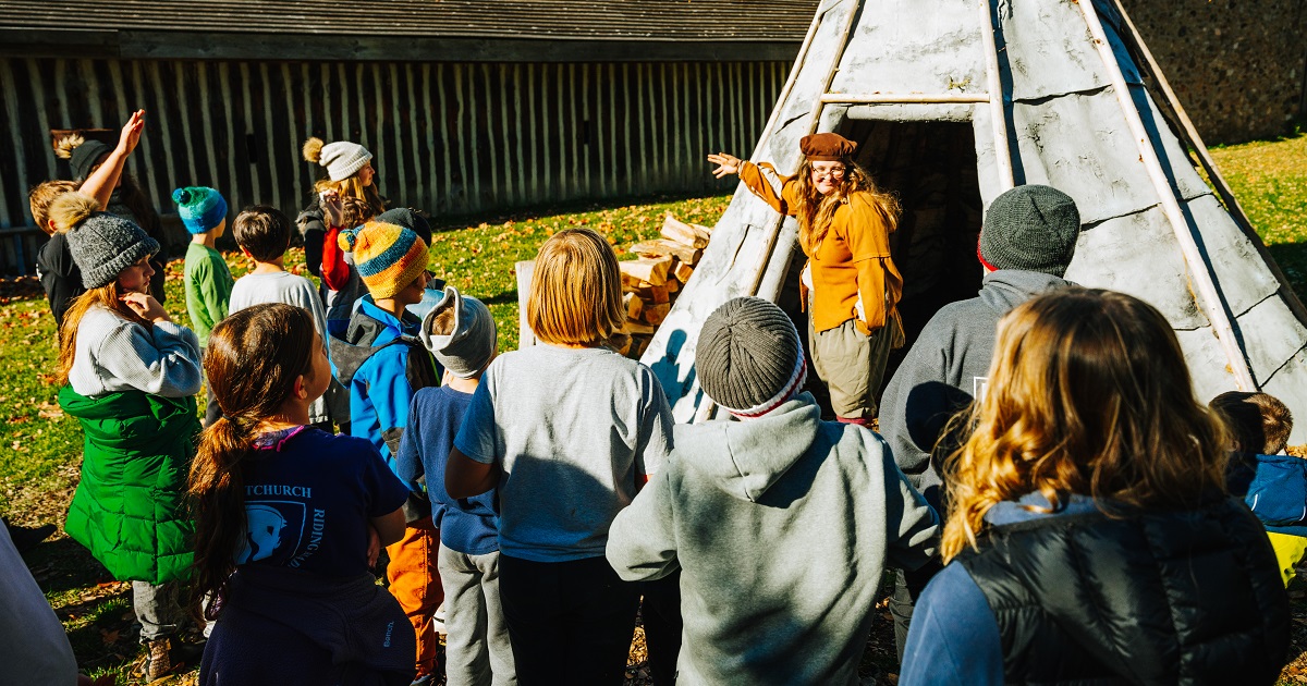 Hope, a costumed interpreter at Sainte-marie, entertaining a group of students outside of the main entrance wigwam