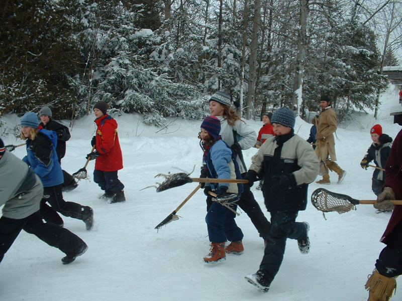Students in snowsuits running with lacrosse sticks at Sainte-Marie