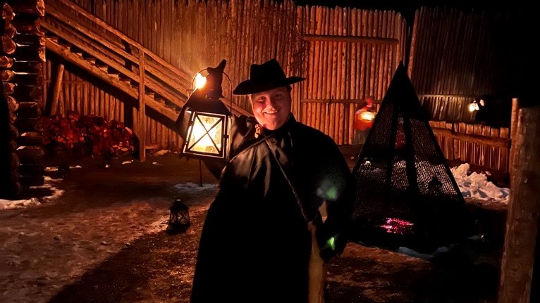 A historical interpreter holds up a lantern with a snowy backdrop