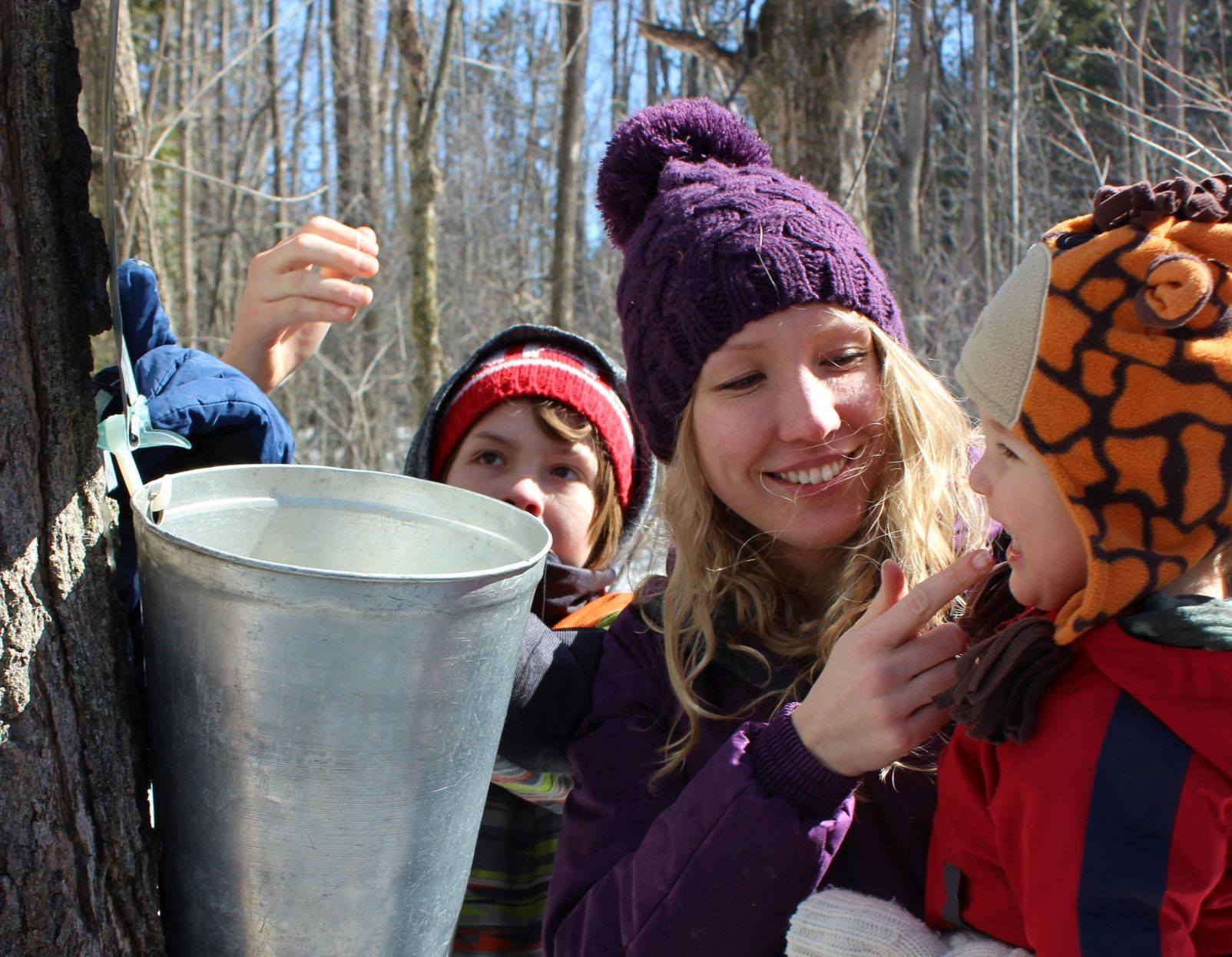 A mom invites her young son to taste sweetwater from a bucket