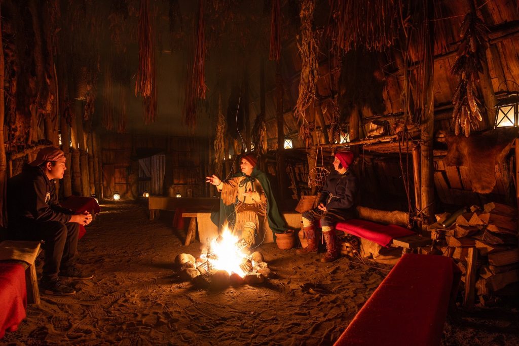A storyteller in the longhouse in the evening, with a fire roaring