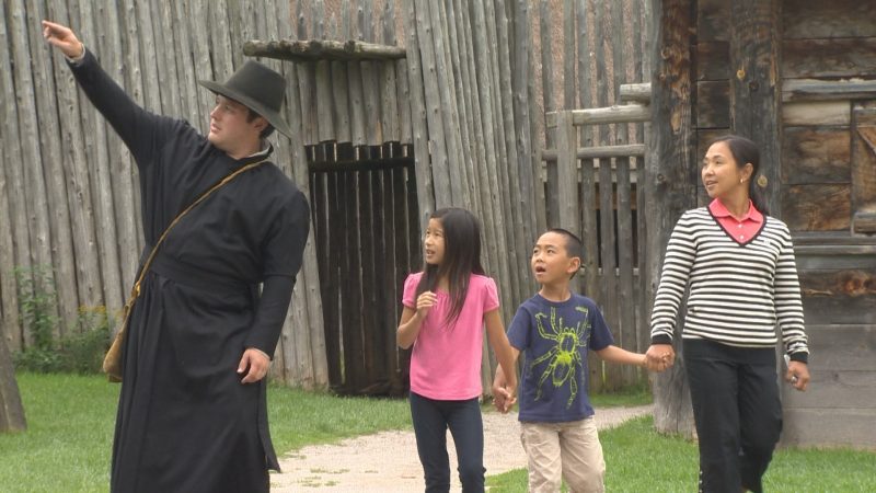 A costumed interpreter guides a family on a walking tour of Sainte-Marie