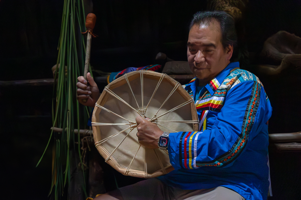 Chris walser holds a drum in the longhouse at Sainte-Marie