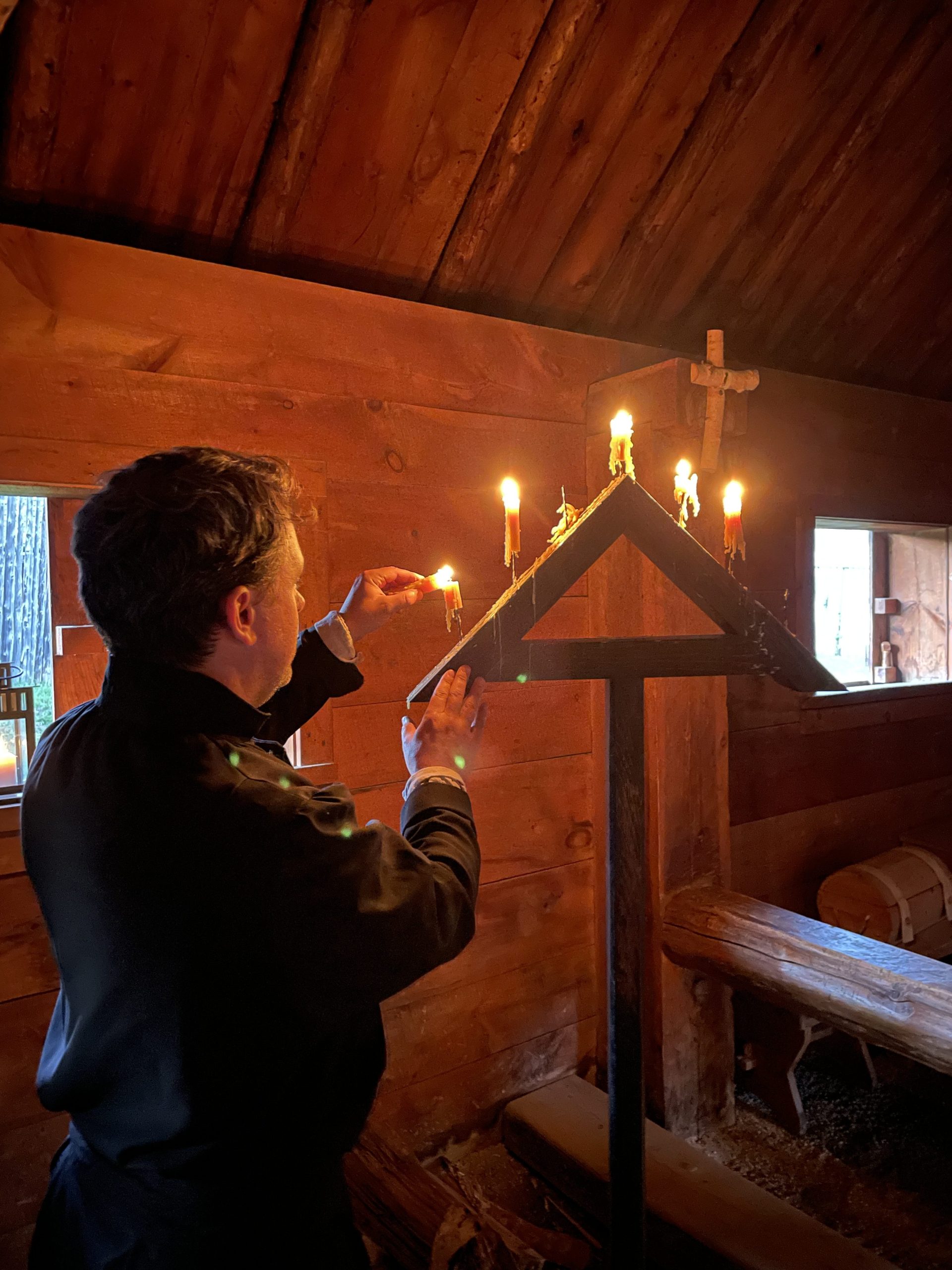 A historical interpreter lights candles in the Church of Saint-Joseph at dusk