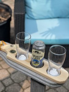Wooden beer flight board with empty glasses and one can of beer in the middle on Muskoka chair arm