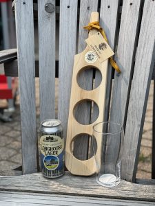 Wooden beer flight board with beer can next of it on Muskoka chair