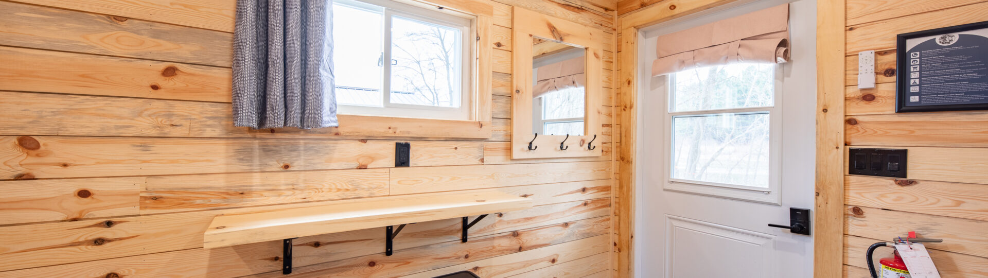 Cozy cabin interior with wood paneling, a door and windows, and a small table with two stools.