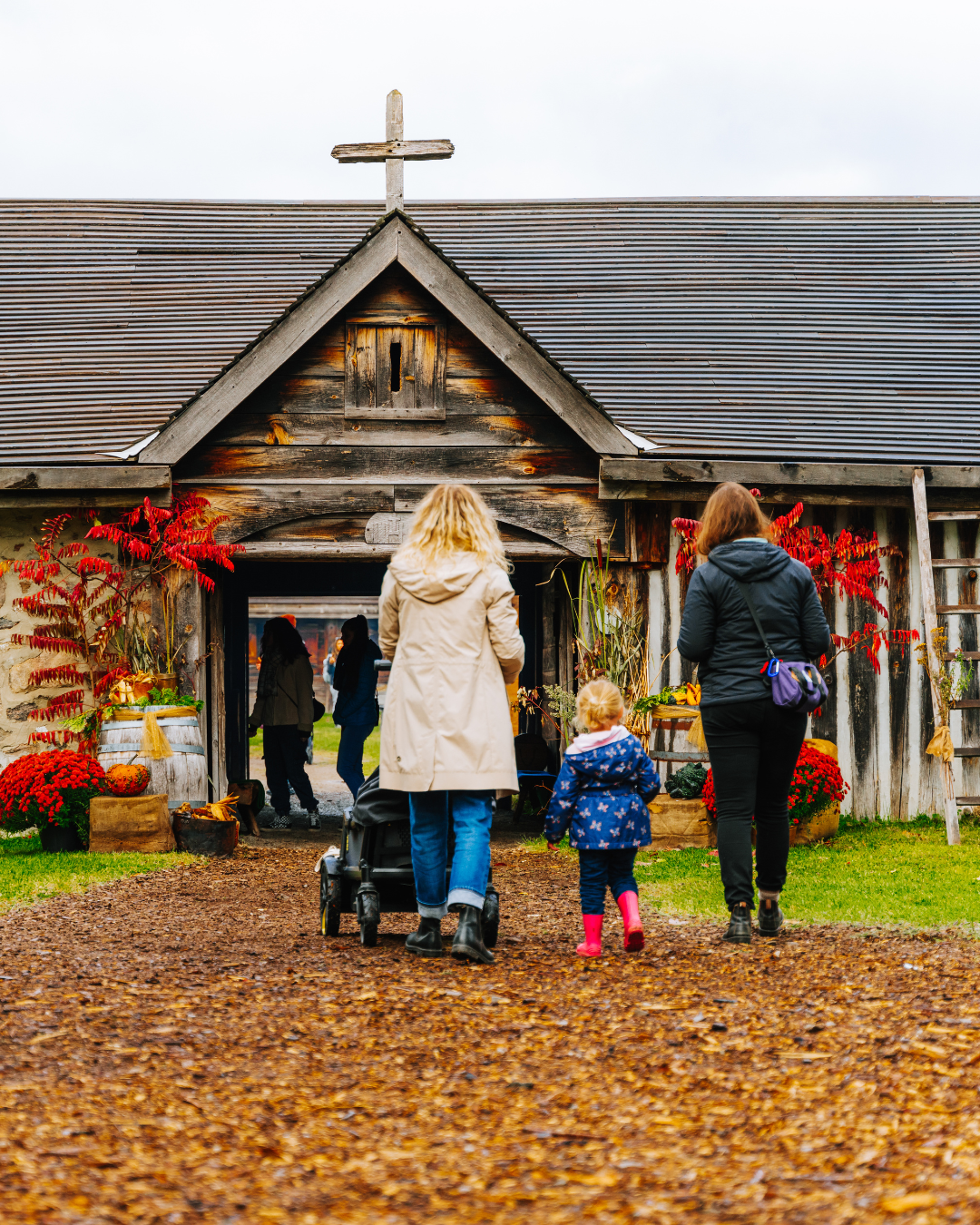 A small family walking onto Sainte-Marie historic site with fall decor