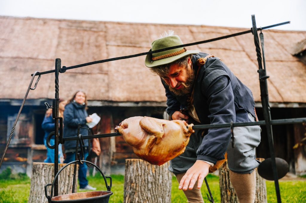 A costumed interpreter roasts a chicken over a fire