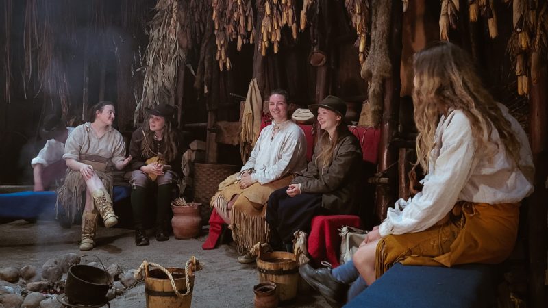Historical interpreters laugh and chat inside a longhouse