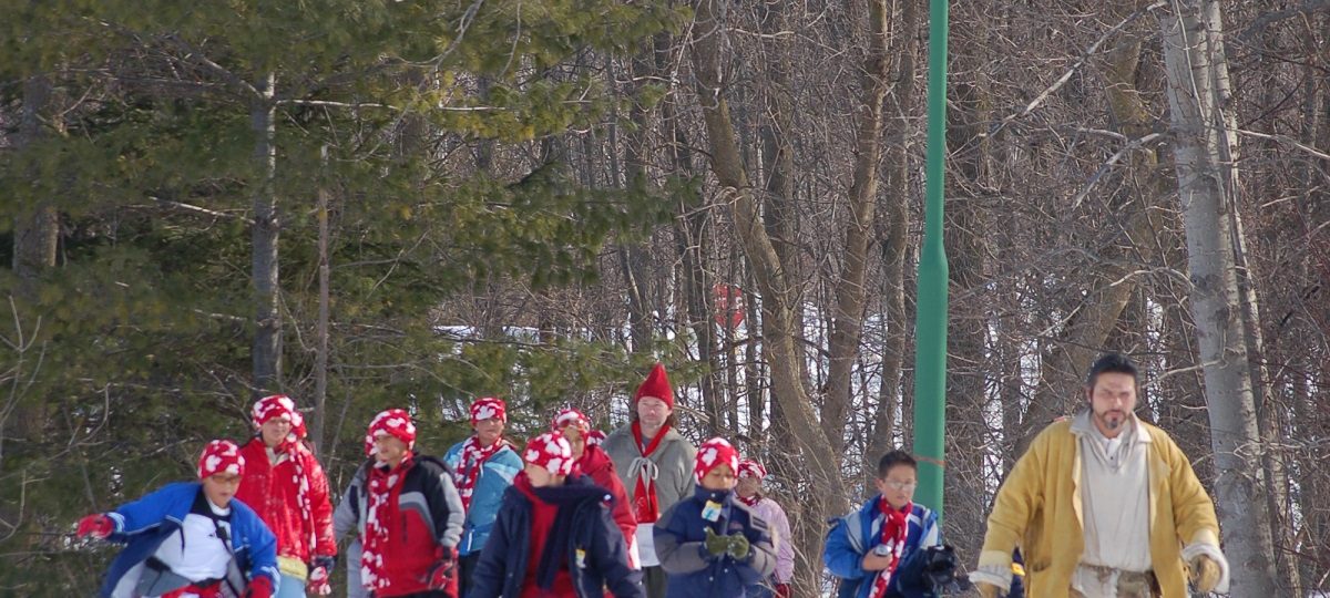 An indigenous historical interpreter leads a group of young students on a snowshoe through nearby woods