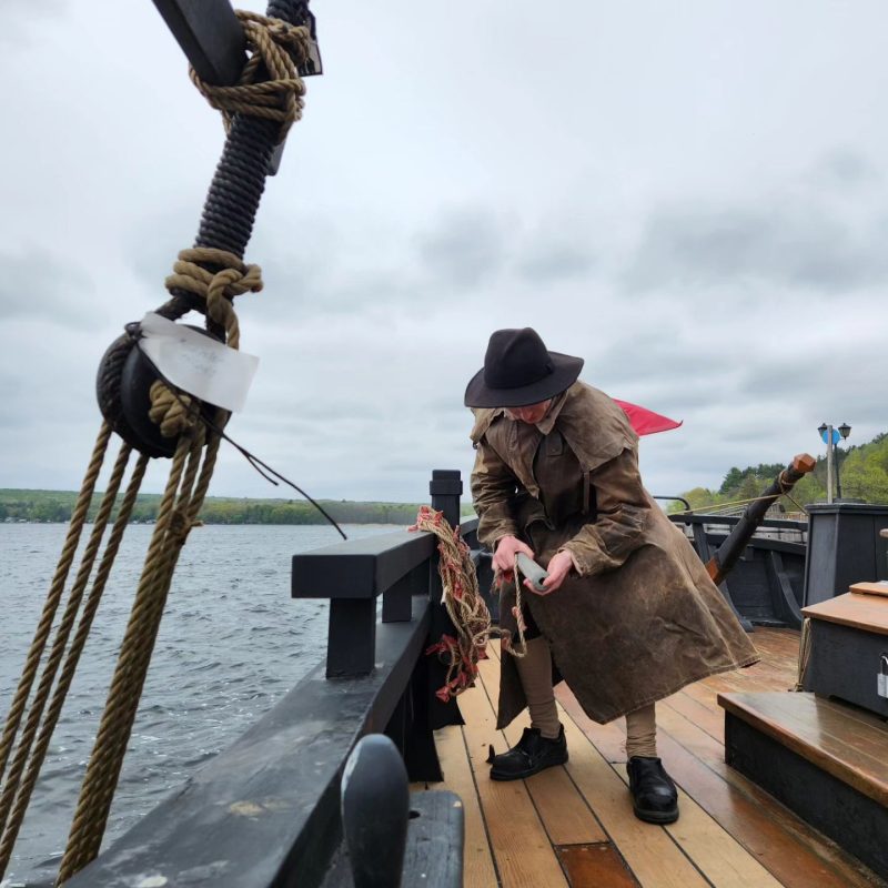 A history interpreter wears a canvas rain coat on a ship