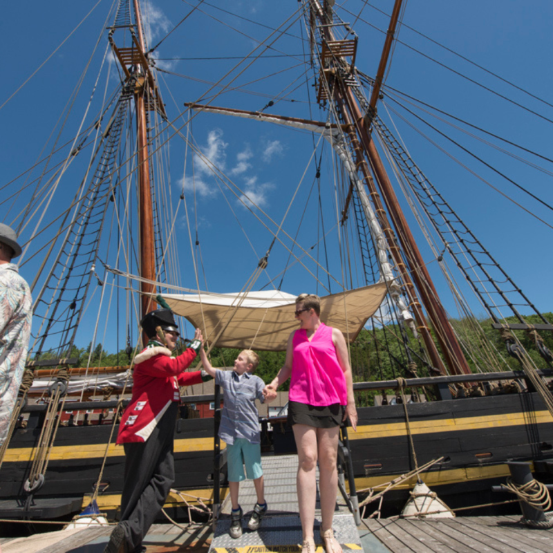 Guests high fiving a historical interpreter dressed as a solder, in front of the rigged HMS Bee